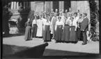 'Från ''Sommarkursen'' på  gamla museet, sommaren 1916. Gruppbild med kursdeltagarna, med knappt 30 kvinnor och män,  på gården med Leonard Axel Jägerskiöld i mitten. Kläder. Museivakten Sally Benedikta Olander längst till vänster i mörk klädsel. Till höger om Jägerskiöld står lektor W. Björck och till vänster om honom snett ovanför står museivakten, vaktmästaren Anders Svensson. ::  :: Ingår i serie med fotonr. 737-740.'