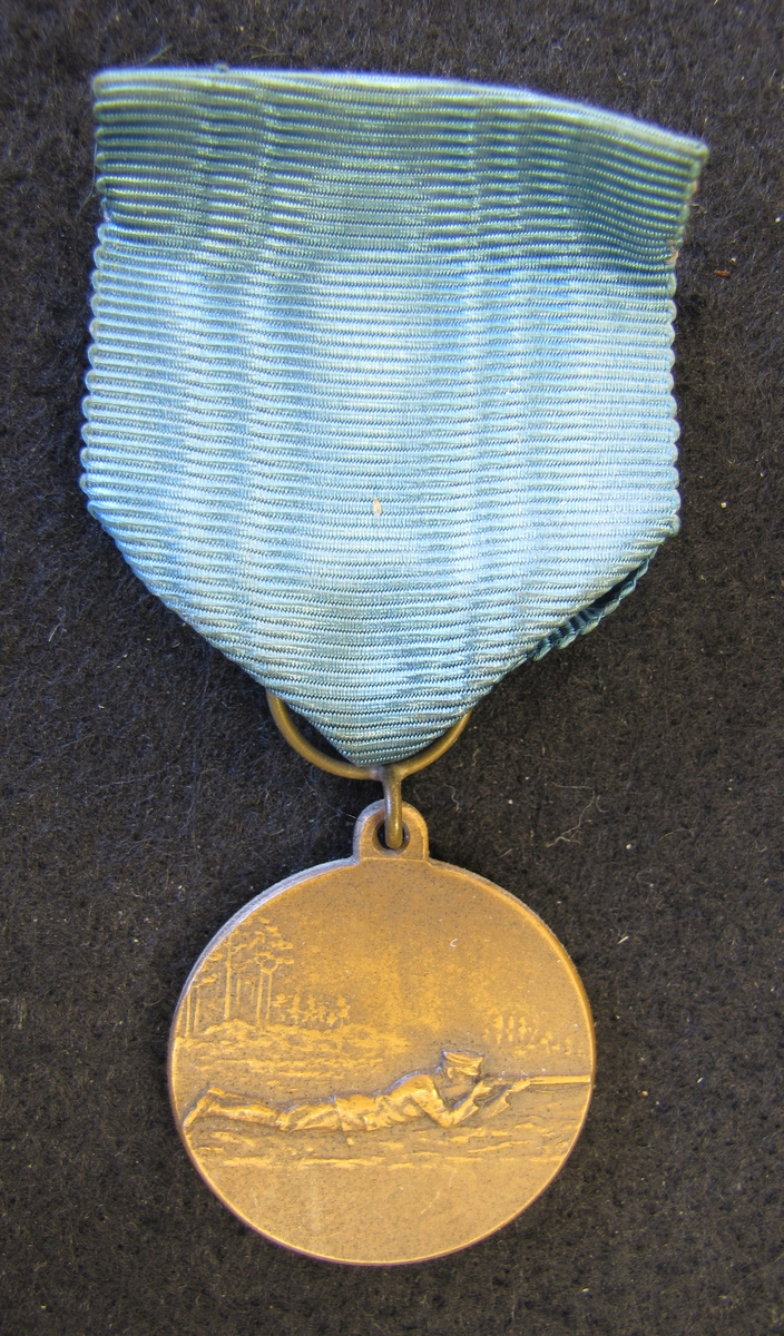Medalj med sidenband i blått.

På åtsidan ligger en man sikande med gevär. På frånsidan en lagerkrans.

Medaljen ingår i en samling märken och medaljer sittande på en tavla med märken, framförallt skyttemärken.

Karl-Fredrik Nyström var aktiv fritidsskytt och var en av de drivande för att starta Vänersborgs skytteklubb.