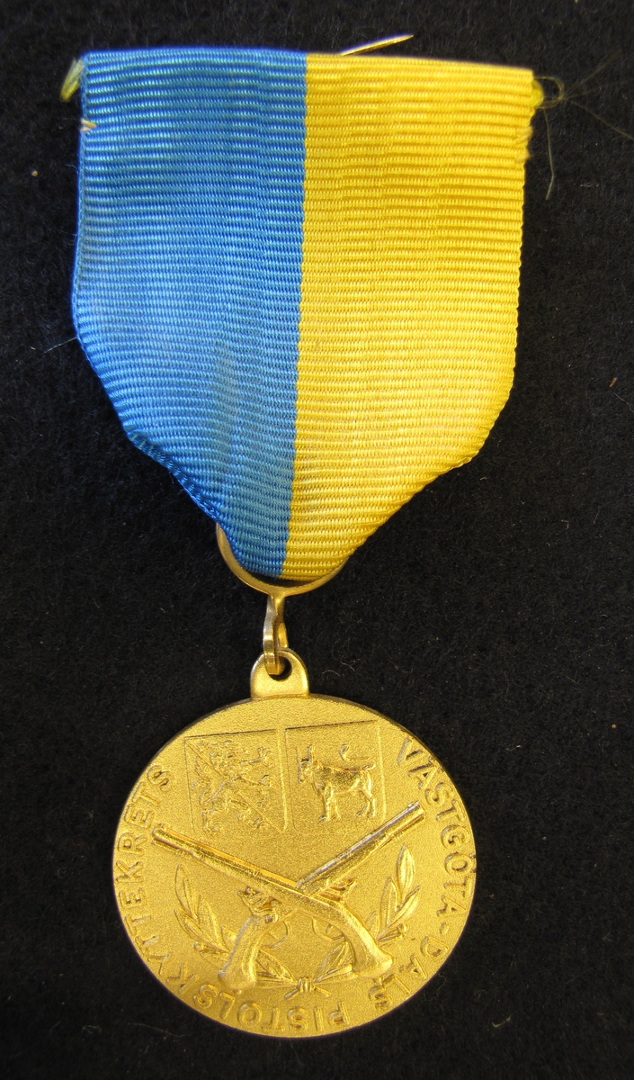 Medalj med sidenband. Västergöta-Dals pistolskyttekrets medalj tilldelad Karl-Fredrik Nyström. 5 K-F Nyström för förtjänst 1978.

På åtsidan finns två korslagda pistoler. Bakom dem finns en lagerkrans. Ovanför två sköldar, en med Västergötlands vapen och den andra en med Dalslands vapen. Runt kanten står Västgöta-Dals pistolskyttekrets.

Medaljen ingår i en samling märken och medaljer sittande på en tavla med märken, framförallt skyttemärken.

Karl-Fredrik Nyström var aktiv fritidsskytt och var en av de drivande för att starta Vänersborgs skytteklubb.