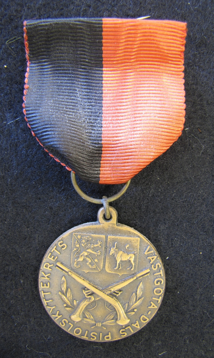 Medalj med sidenband. Medalj från Västgöta-Dals pistolskyttekrets tilldelad Karl-Fredrik Nyström. 7 Pluton Kretsmästare Fältskjutning 1956.

På åtsidan finns två korslagda pistoler. Bakom dem finns en lagerkrans. Ovanför två sköldar, en med Västergötlands vapen och den andra en med Dalslands vapen. Runt kanten står Västgöta-Dals pistolskyttekrets.

Medaljen ingår i en samling märken och medaljer sittande på en tavla med märken, framförallt skyttemärken.

Karl-Fredrik Nyström var aktiv fritidsskytt och var en av de drivande för att starta Vänersborgs skytteklubb.