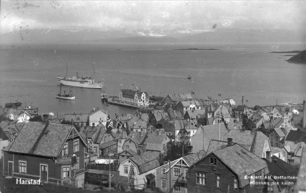 Postkort med motiv som viser utsikt over Harstad sentrum, med fartøyer ved dampskipskaia i bakgrunnen.