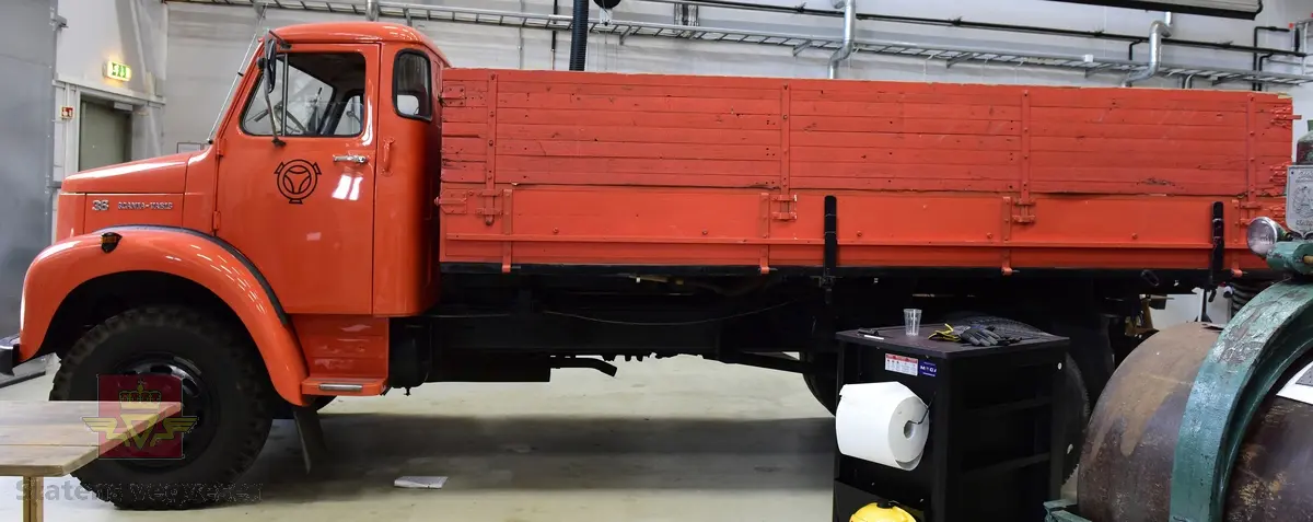 Lastebil på 6 hjul, (to akslet) med bakhjuls drift. Akselavstand 4,2 meter.  I hovedsak oransje. Motoren er en turbomatet 4-sylindret dieselmotor av typen Scania-Vabis DS5, den yter 120 hestekrefter og har et sylindervolum på 5193 kubikkcentimeter. Girkassen er en manuell 5-trinns synkronisert utgave, høy- og lavgir i bakakslingen (two-speed) gir tilsammen 10 gir pluss revers. Bremsene er drevet av trykkluft. Bilen har lasteplan med karmer og et ekstra sett karmer på toppen. Bilen har 3-veis hydraulisk tipp fra Thanstrøm i Halden. Svart interiør, lakkert grå innvendig. Egenvekten er ca. 5,1 tonn, lasteevne ca. 5,825 tonn. Totalvekt 11 tonn.
Farge: paprika rød.