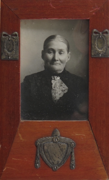Kvinneportrett. Foto en face, midtskill og glatt hår, sort mønstret kjole med gullbrosje  AAM.11 413 over fichu.