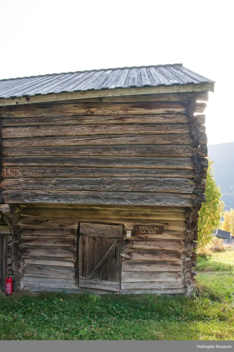 Dette er en stall med trev.  Den er sammensatt av flere tømmerhus som trolig er bygd en gang mellom 1825 og 1850 her på Skaga.  Annen etasje er utkraget og den har bordtak.