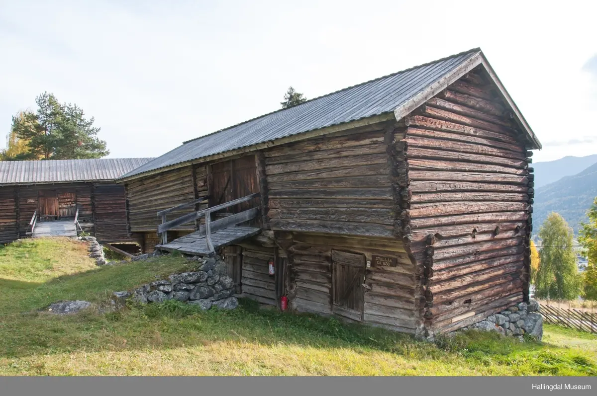 Dette er en stall med trev.  Den er sammensatt av flere tømmerhus som trolig er bygd en gang mellom 1825 og 1850 her på Skaga.  Annen etasje er utkraget og den har bordtak.