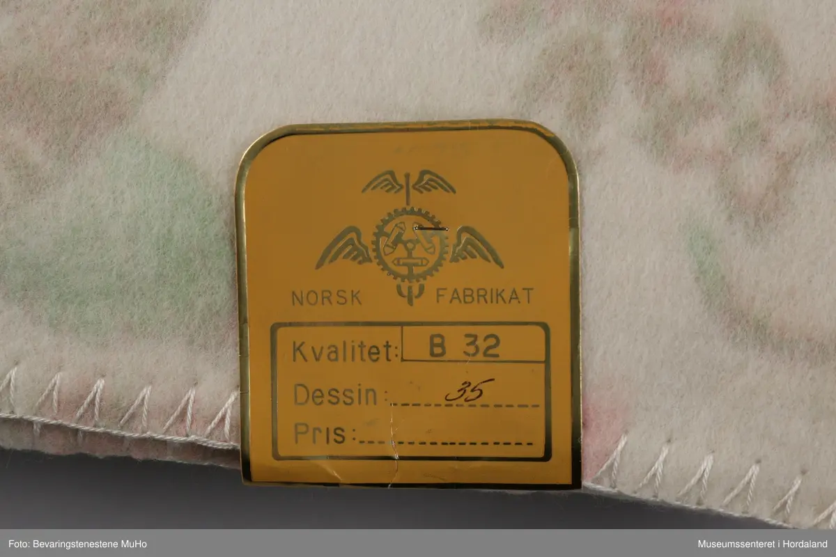 Rektangulært ullteppe i åpnet plastemballasje.