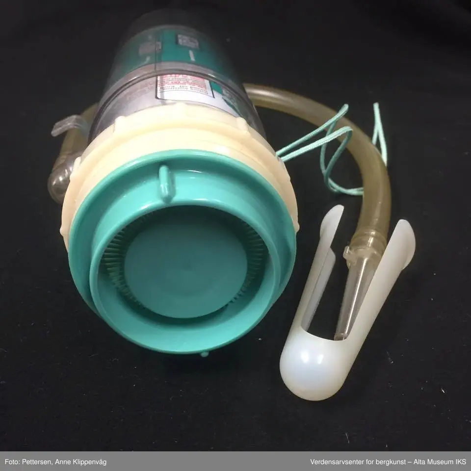 A. Sylinderformet plastapparat med tilfestet gummislange og gjennomsiktig plasttut.  Inneholder en driftspatron fylt med ufarlig gass.
B Rektangulært hefte, bruksanvisning.