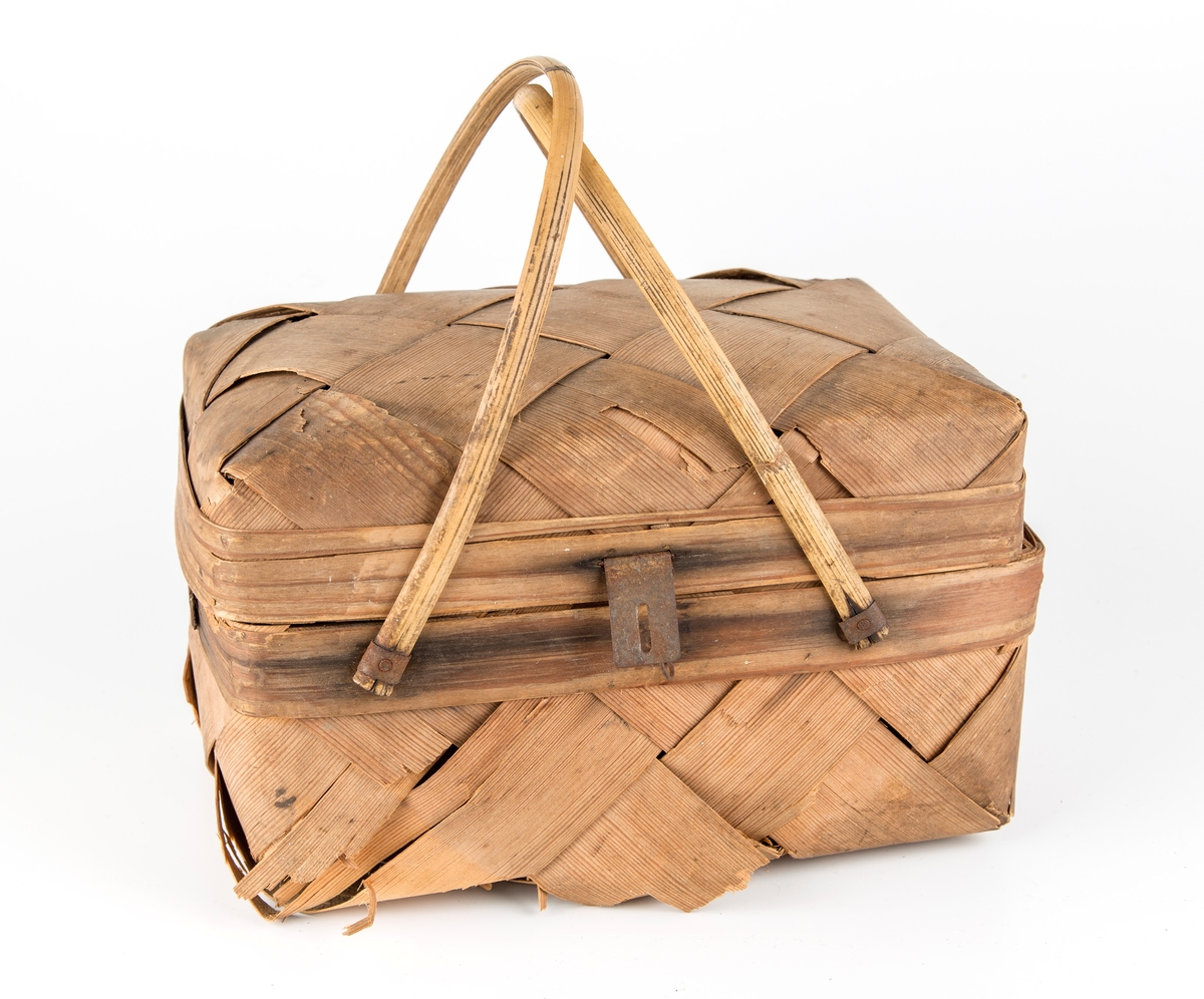 Rektangulær kurv, skråflettet av brede spon. Hengslet lokk, 2 hanker.