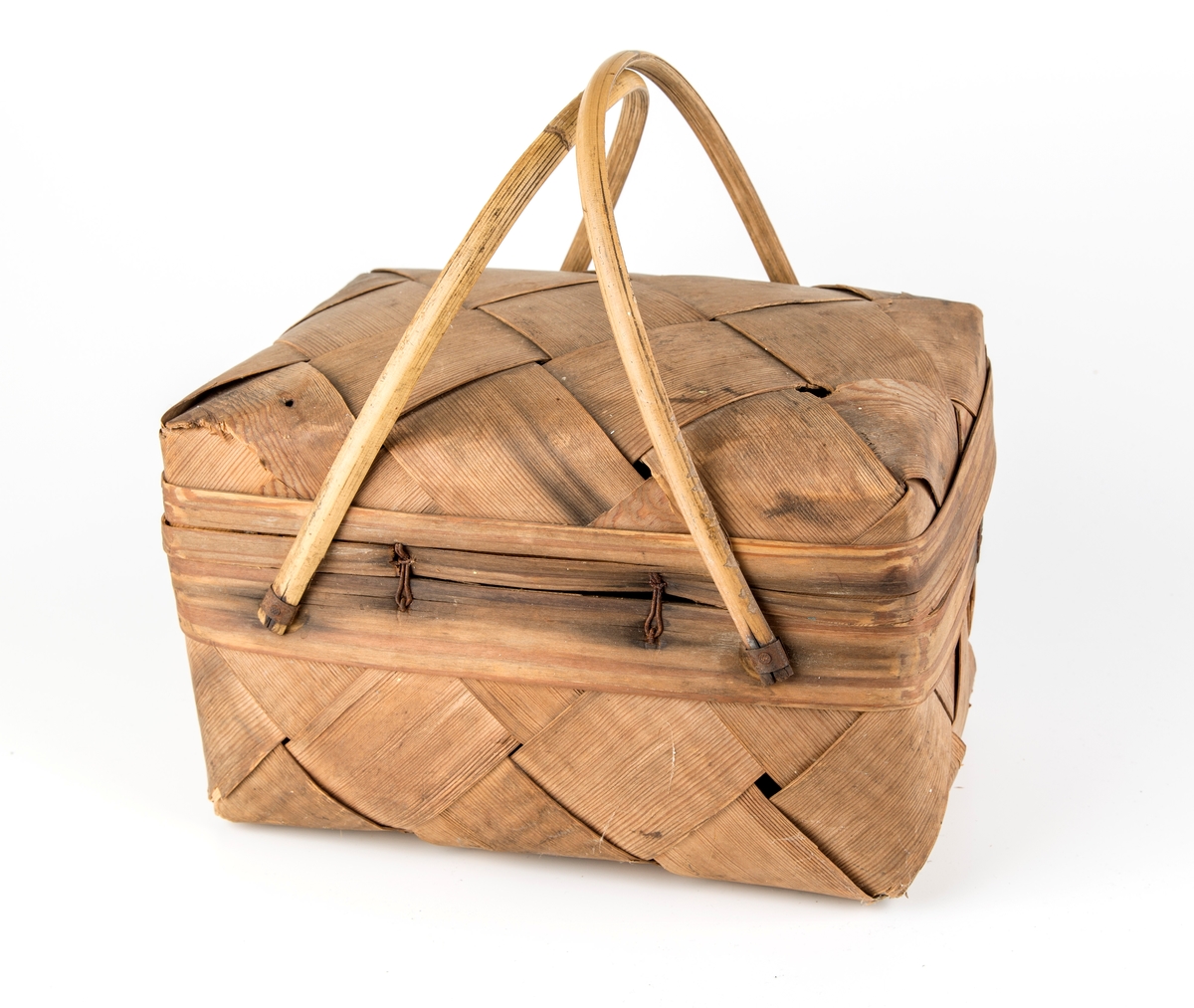 Rektangulær kurv, skråflettet av brede spon. Hengslet lokk, 2 hanker.