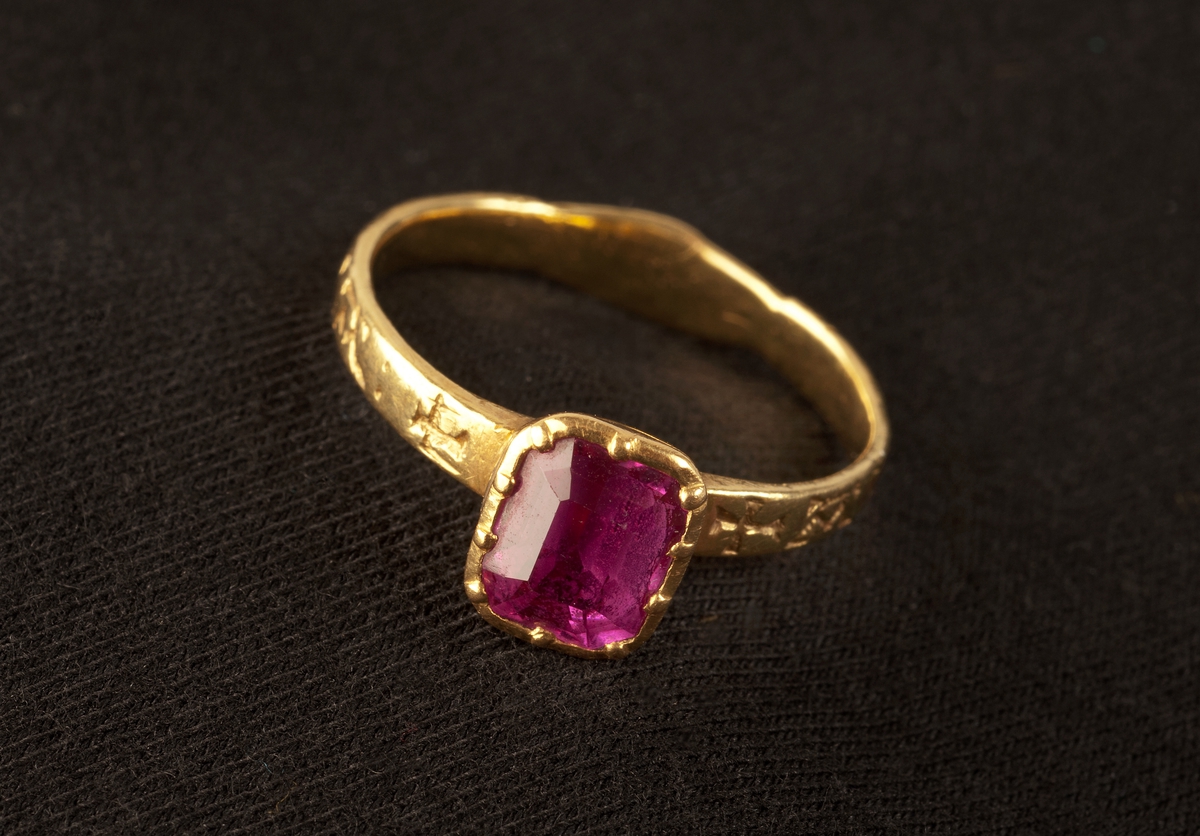 Fingerring av guld med infattad röd sten och handslag på skenans baksida. På ringens utsida ingraverat  AVEM ARIA ( d.v.s. AVE MARIA) och två likarmade kors. Tillhörande etui UM20676b.

Didners lät sätta in den ljusröda rubinen.