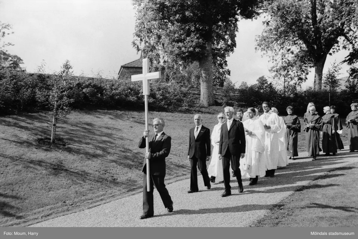 Invigning av den nyare delen av Kållereds kyrkogård år 1983. "Kyrkovaktmästare Knut Lundgren håller ett träkors och leder processionen från Kållereds kyrka till den nya delen av kyrkogården." Efter Knut går, sett från vänster, kyrkvärdarna Elof Johansson och Stig Eklund.