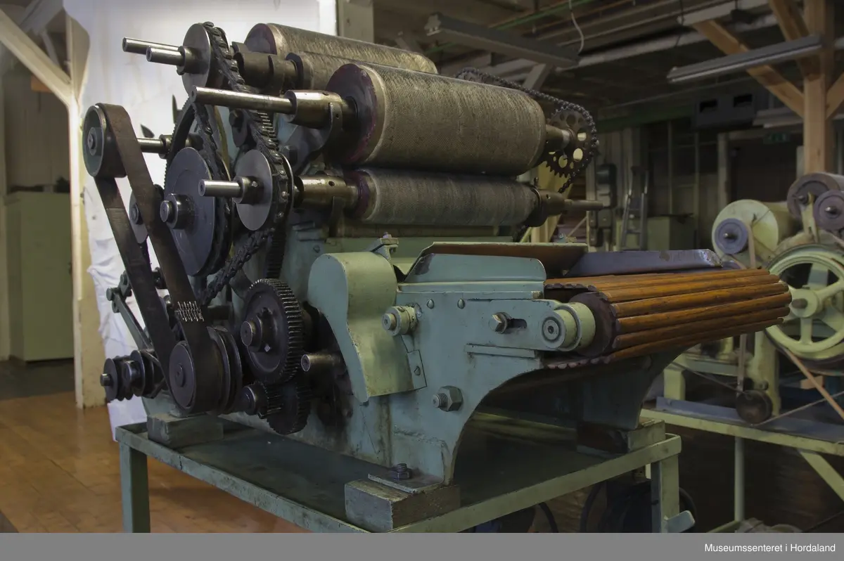 Mintgrøn prøvekardemaskin med tredetaljar, montert på stativ. Ukjend fabrikat.