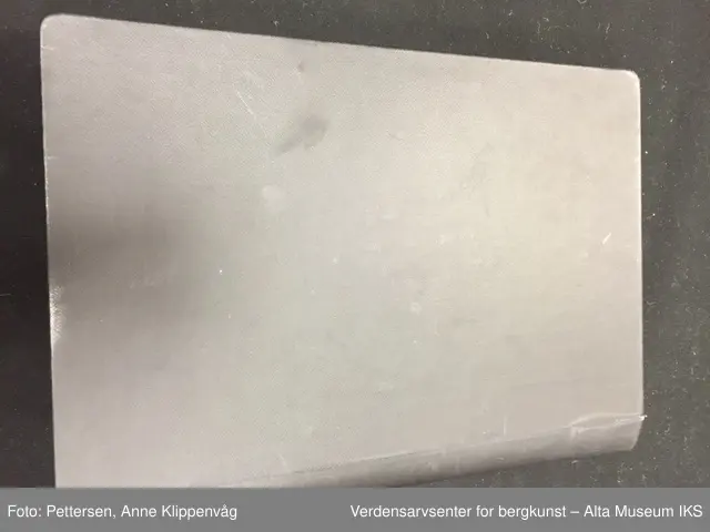 En rektangulær mappe i sort skinn som kan åpnes som en bok. På hver permside er det rammer i metall. I hver ramme er det 33 plastlommer med pappforing. På toppen av hver permside er det en lapp i sort skinn som skjuler den første plastlommen. Under skinnlappen på venstre permsiden er det liten bunke med gule arkivlapper som er håndskrevet på.