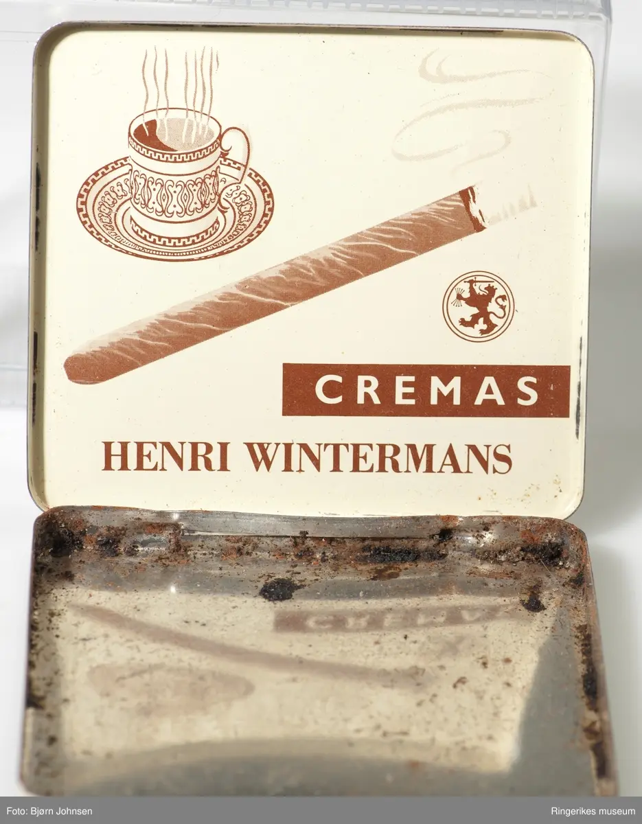 På fronten av  lokket: A- dampende sigarillo, løve med hellebard i en oval logo med en stilisert krone over; B - stilsvarende sigarillo, en mindre logo og en kaffekopp med skål,  fylt med rykende varm kaffe.