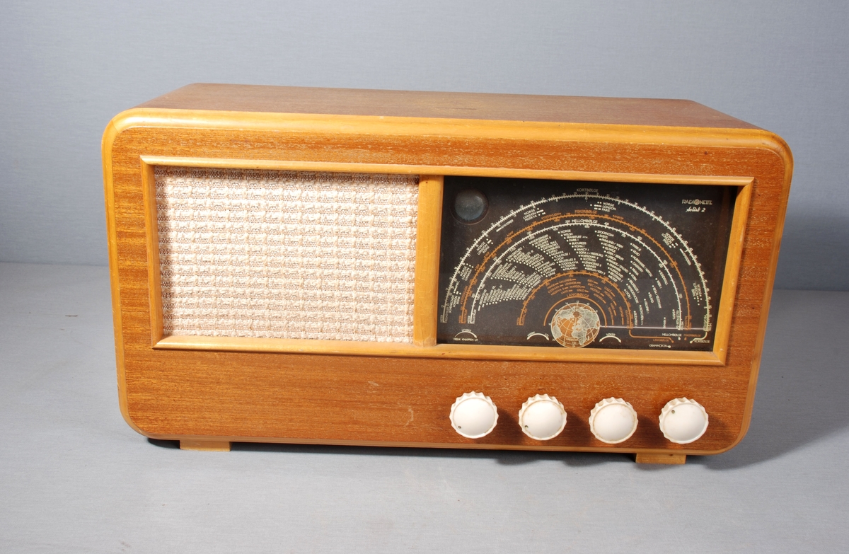 Radiomottaker for kort-/mellom- og langbølgemottak. Rektangulær kasse med åpning for høyttaler dekket av tekstil på framsiden. Ved siden av stasjonsvelger med viser på skala. Knapper for regulering av lydstyrke, lysstyrke, søk og valg av frekvensbånd/grammofon. På baksiden kontakt for antenne, jord og grammofon. Merkelapp for betalt stempelavgift, og skilt med wattstyrke. Tegning av kretskort. Til ledningen er festet en eske med Mullard radiorør. Kabel med støpsel på baksiden