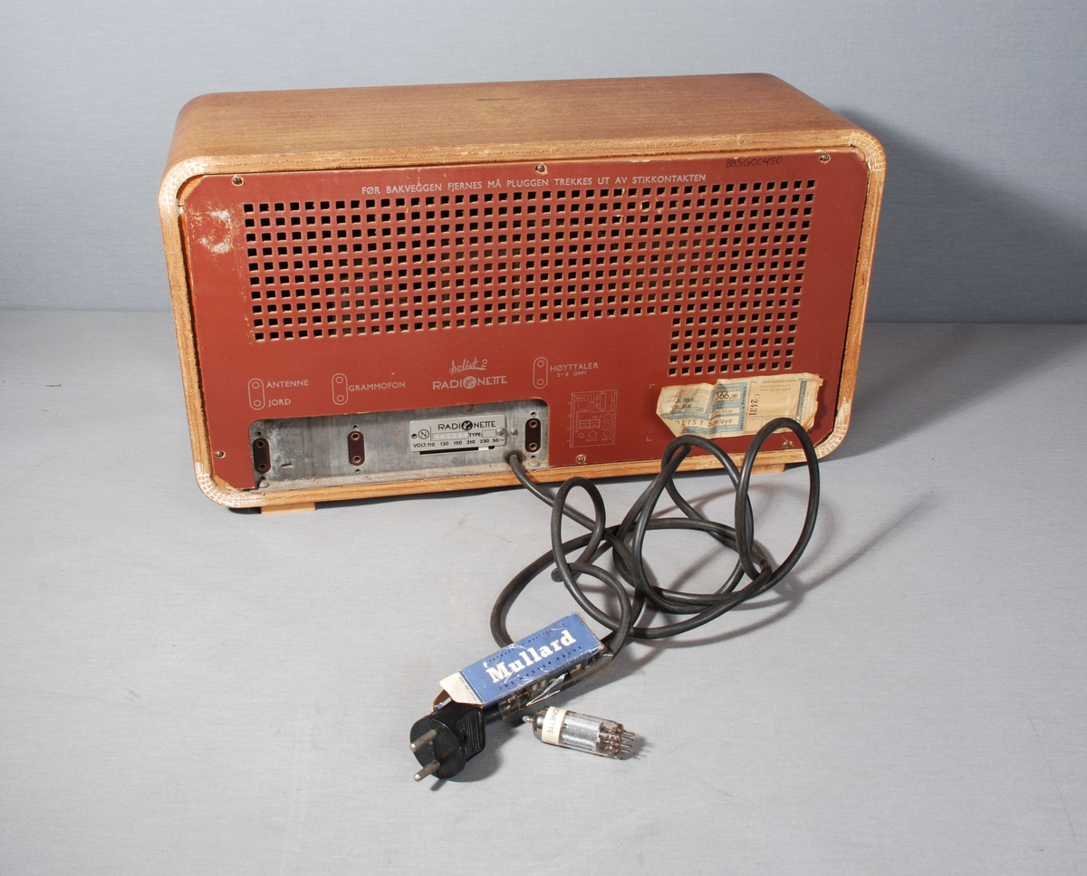 Radiomottaker for kort-/mellom- og langbølgemottak. Rektangulær kasse med åpning for høyttaler dekket av tekstil på framsiden. Ved siden av stasjonsvelger med viser på skala. Knapper for regulering av lydstyrke, lysstyrke, søk og valg av frekvensbånd/grammofon. På baksiden kontakt for antenne, jord og grammofon. Merkelapp for betalt stempelavgift, og skilt med wattstyrke. Tegning av kretskort. Til ledningen er festet en eske med Mullard radiorør. Kabel med støpsel på baksiden