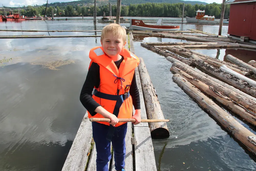 Gutt med redningsvest bruker fløterhake på tømmeret i elva