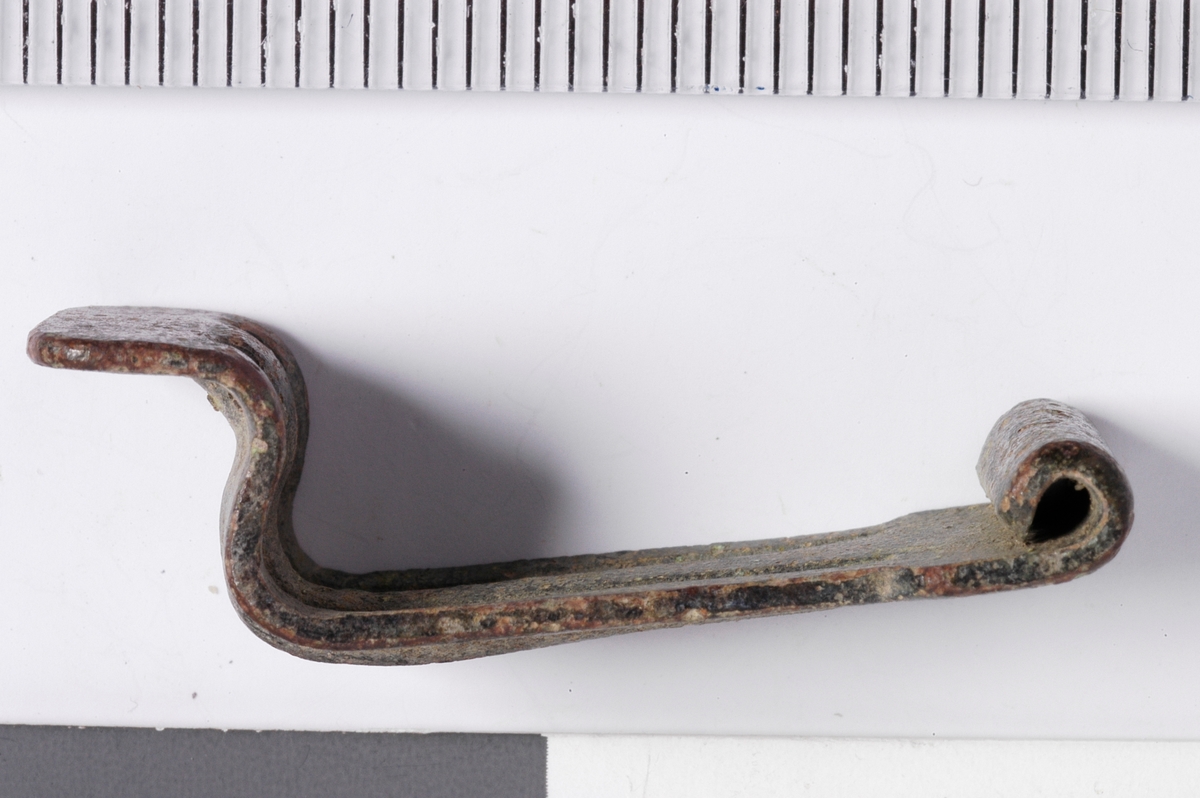 MALV: L. 31  B. 11 MM, BÅNDFORMET MED ENE ENDE OMBØYET TIL HENGSLE OG ANDREBØYET TIL EN ENKEL HEMPE. DEKOR: 2 LINJER I RELIEFF. 
