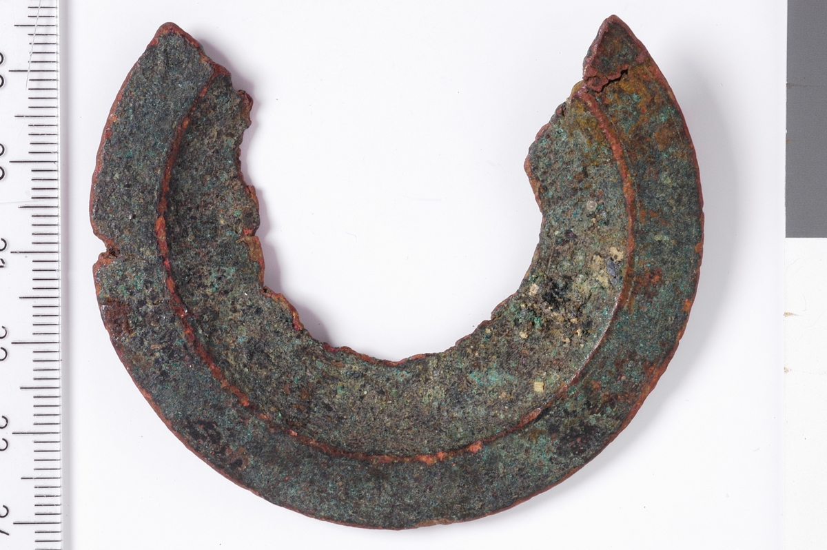Sirkelformet metallplate med jevn ytterkant og en bruddfalte klangs hele innsiden, samt i begge kortender. det er ingen tegn til dekor, men platen er flat i ytterkant og har deretter en konveks bue som går innover. Dette er et kraftig beslag, men med ukjent bruksområde.