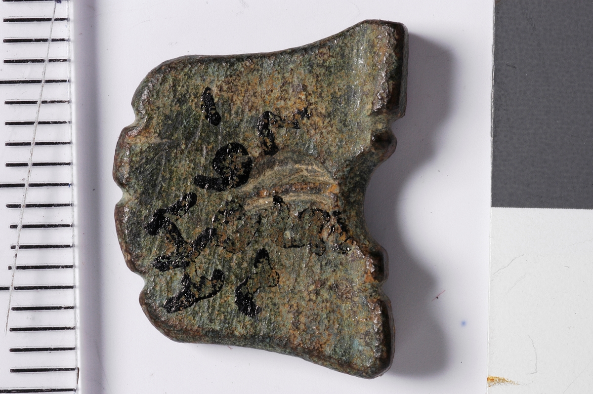 Tilnærmet firkantet gjenstand med en halvsirkelformet fordypning i den tykkeste enden. Denne enden fungerer som en "fot" som gjør at gjenstanden står stabilt oppreist. Tykkelsen er avsmalnende opp fra foten. Alle sider er intakte og toppen, dvs motsatt ende av foten, er bearbeidet med tre fordypninger som gir en bølgeform. Midt i overflaten av gjenstanden, rett over buen, sees på den ene siden rester av en fordypning som kan ha vært et preg. Kan være en spillebrikke.