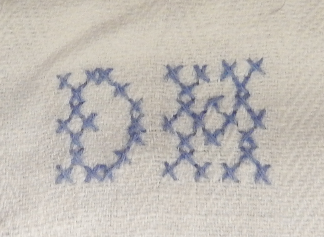 En dokkeseng i kurvfletting fra ca. 1905, med løse sengegavler, en madrass, et laken (glasshånklr med monogram), en overmadrass, to puter, med putevar, en dyne og et heklet sengeteppe.