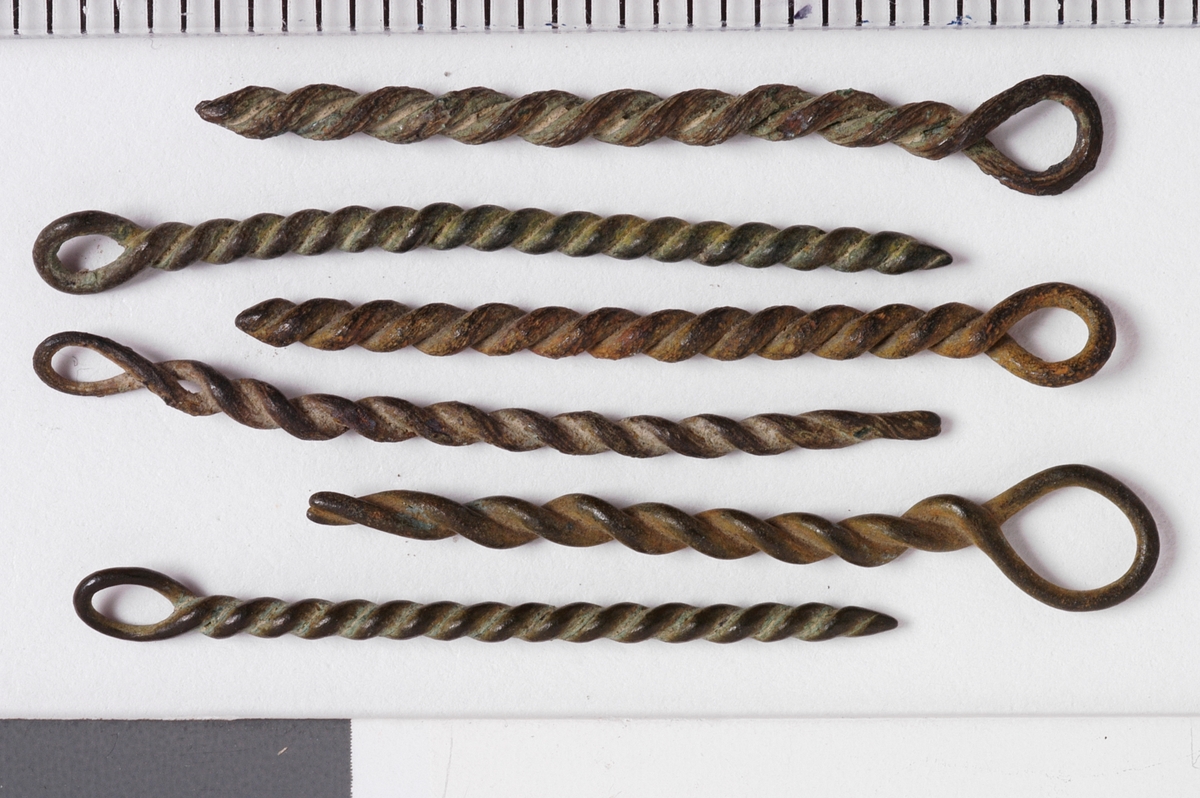 MALV: SE BESK., ST. L. 45 MM, MINSTE L. 16 MM, ST. DIAM. 2 MM, MINSTEDIAM. 1 MM. LAGET AV METALLTRÅD. GJENSTANDEN DANNET VED AT TYNNMETALLTRÅD (DIAM. 0, 5-1, 1 MM) ER LAGT DOBBEL OG SNODD I SPIRAL. ØYE IENDEN. NB! 2 HAR FLATTRYKT PARTI VED HULLET. 