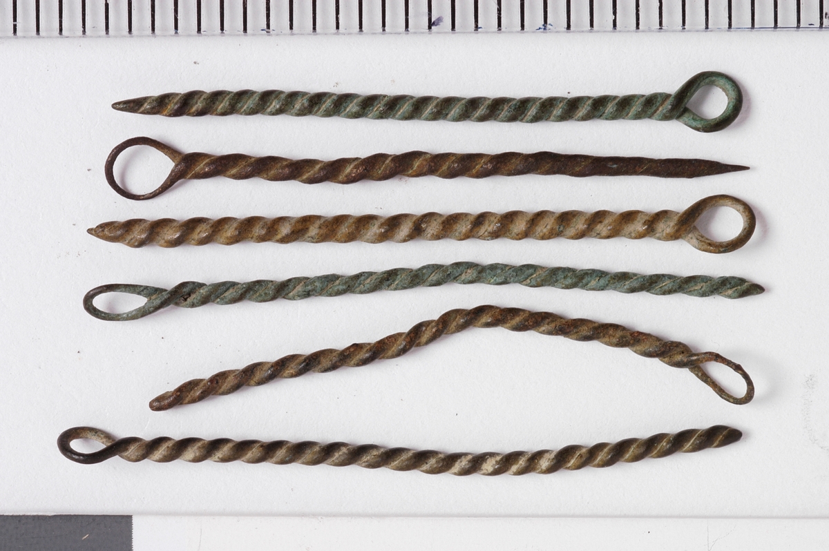 MALV: SE BESK., ST. L. 45 MM, MINSTE L. 16 MM, ST. DIAM. 2 MM, MINSTEDIAM. 1 MM. LAGET AV METALLTRÅD. GJENSTANDEN DANNET VED AT TYNNMETALLTRÅD (DIAM. 0, 5-1, 1 MM) ER LAGT DOBBEL OG SNODD I SPIRAL. ØYE IENDEN. NB! 2 HAR FLATTRYKT PARTI VED HULLET. 