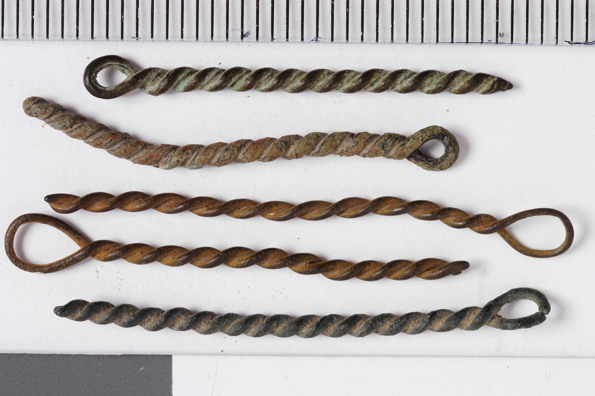 MALV: SE BESK., ST. L. 45 MM, MINSTE L. 16 MM, ST. DIAM. 2 MM, MINSTEDIAM. 1 MM. LAGET AV METALLTRÅD. GJENSTANDEN DANNET VED AT TYNNMETALLTRÅD (DIAM. 0, 5-1, 1 MM) ER LAGT DOBBEL OG SNODD I SPIRAL. ØYE IENDEN. NB! 2 HAR FLATTRYKT PARTI VED HULLET. 
