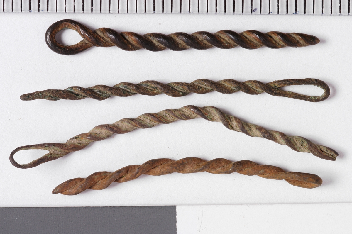 MALV: SE BESK., ST. L. 45 MM, MINSTE L. 16 MM, ST. DIAM. 2 MM, MINSTEDIAM. 1 MM. LAGET AV METALLTRÅD. GJENSTANDEN DANNET VED AT TYNNMETALLTRÅD (DIAM. 0, 5-1, 1 MM) ER LAGT DOBBEL OG SNODD I SPIRAL. ØYE IENDEN. NB! 2 HAR FLATTRYKT PARTI VED HULLET. 