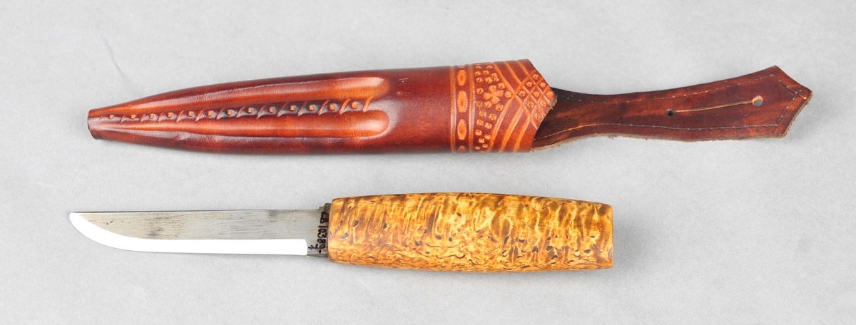 Handtaket er av olja valbjørk, utan holkar.Smidd blad med stempel. Slira er sauma kant i kant. Dekoren er trykt og pauta.