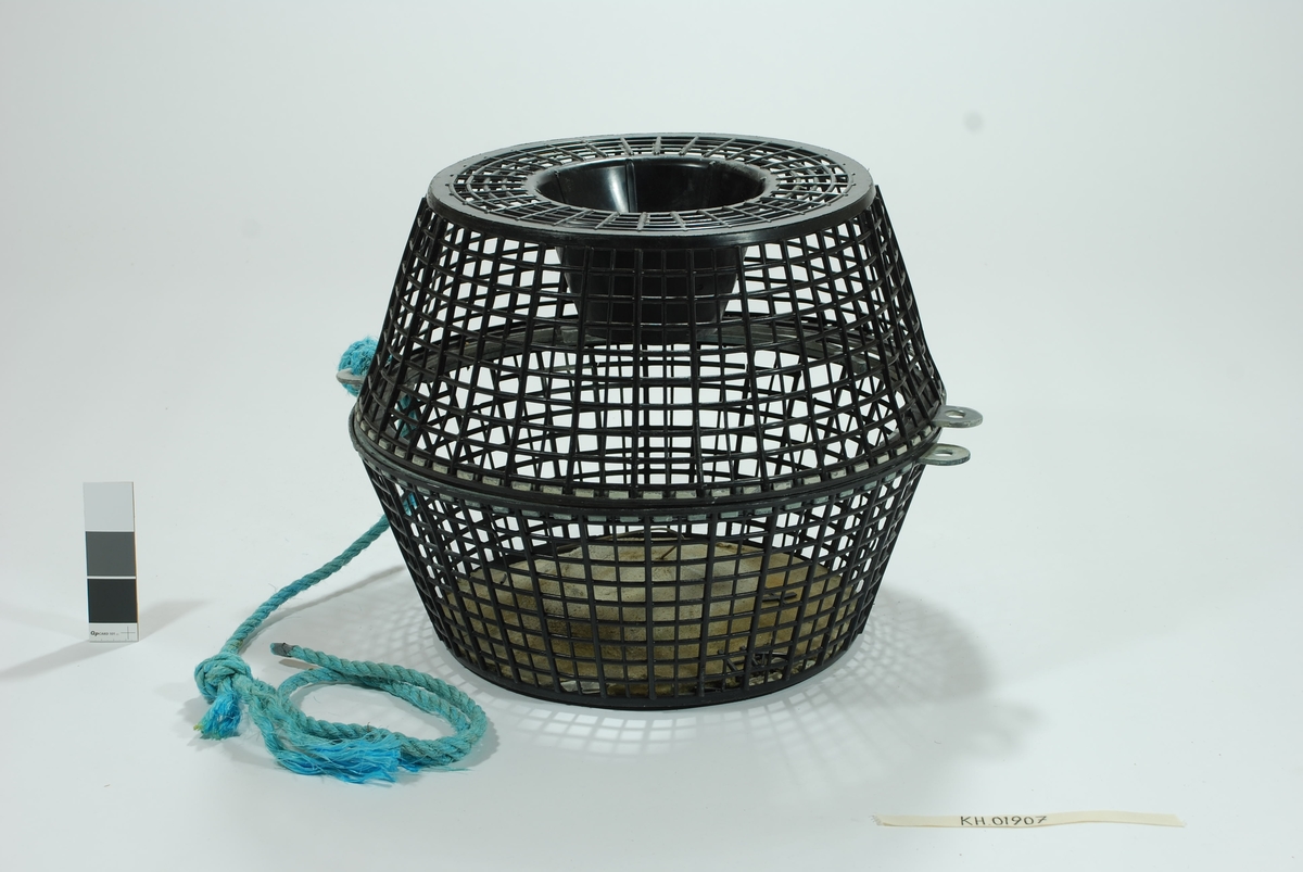 En forenklet versjon av de tradisjonelle fall-fellene hvor garnet er erstattet av hård-plast. Todelt bøtte-tene med topp og bunn. Form og materiale kan minne om en skittentøyskurv. 
Rutemønstret, sort hardplast. 
Betongblokk i bunnen til synkemateriale. Dekker hele bunnen. Små biter faller av i kantene.  Agnspyd av metall er støpt inni betongen. Fallbøtte i toppen. Både topp og bunn har randkant i hard gummi med tapper som vris i hverandre for å lukke tena. Turskis nylontau er festet i disse.