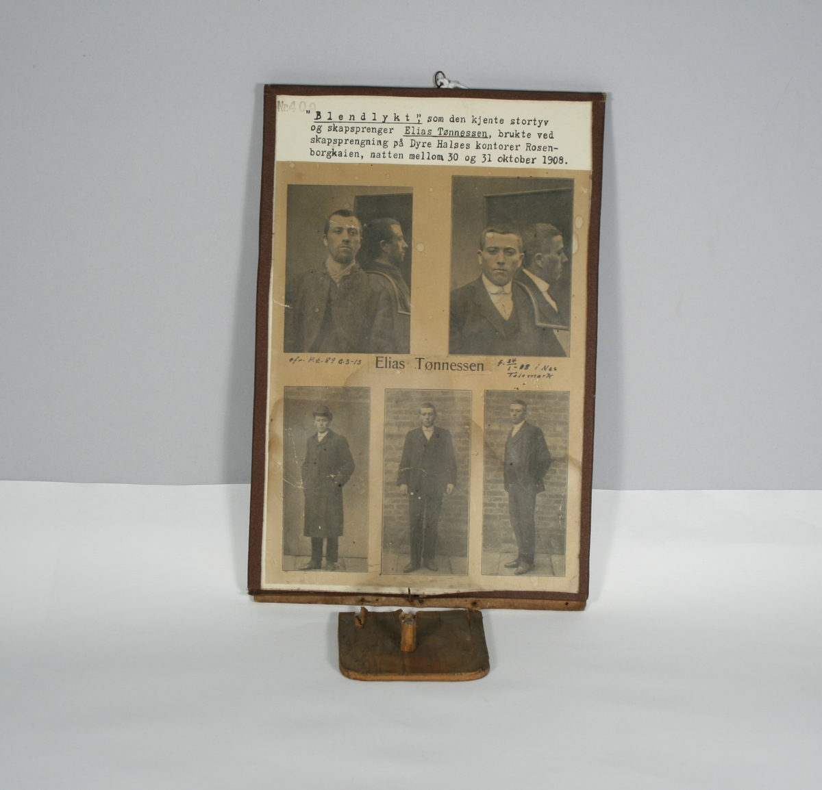 Montasje med 5 foto av Elias Tønnesen på en plate. Platen med bilder og tekst har nederst en påfestet plate for utstilling av "lykten", som er en sekskantet teboks, dekorert med blomster, og med to små hull for lyset. Teboksen inneholder en talglysstump.