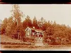 Sommarstugan Fridensborg, envånings sommarstuga med inredd vind och veranda. Ett uthus till vänster. Tre barn och två vuxna framför stugan.
Fotograf Sam Lindskog