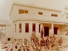 Tvåvånings villa med balkong, burspråk och veranda. Elva byggnadsarbetare framför huset.
Byggmästare Gothard Gustafsson