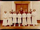 Konfirmander, 7 flickor, 4 pojkar och pastor Gottberg framför Almby kyrkas port.