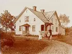 En och en halvvånings bostadshus med veranda och förstubro.
Familj 4 personer framför huset.
Karl Andersson