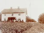 Tvåvånings bostadshus med veranda i snickarglädje.
7 personer framför huset.