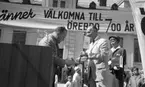 Knytkalaset 5 juli 1965.

Harald Aronsson tilldelas ett standar av en herre med texten 700 år på samt det krönta Ö-et. Jubileumsvärdinna samt publik i bakgrunden.