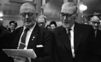 Pensionärspop 2 mars 1966

I förgrunden på bilden syns det två herrar som sitter bredvid varandra. Båda bär glasögon och är klädda i mörka kostymer, ljusa skjortor med mörk slips. Herren som sitter till vänster på bilden håller i sin vänstra hand ett sånghäfte. Han sjunger. I bakgrunden på bilden skymtar det andra herrar och damer. Damerna på bilden bär glasögon och har hattar på sig.