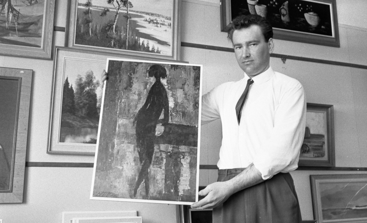 Tavlor 3 maj 1966

Man håller i tavla med abstrakt kvinnomotiv, framför vägg med målningar, mestadels med landskapsmotiv