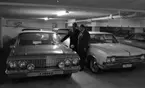 Bilhall 30 mars 1966

Två män står i ett garage och tittar på en bil. En av männen bär kostym. Den andre mannen bär arbetskläder. Andra bilar syns i bakgrunden.