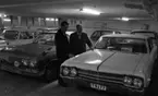 Bilhall 30 mars 1966

Två män står i ett garage och tittar på en bil. En av männen bär kostym. Den andre mannen bär arbetskläder. Andra bilar syns i bakgrunden.