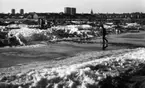 Vår 19 april 1966

En liten pojke går över en vattendränkt gata på våren. Snö ligger fortfarande kvar på marken men håller på att töa bort. Tre andra barn, ett bostadsområde, höghus samt en kyrka syns i bakgrunden.