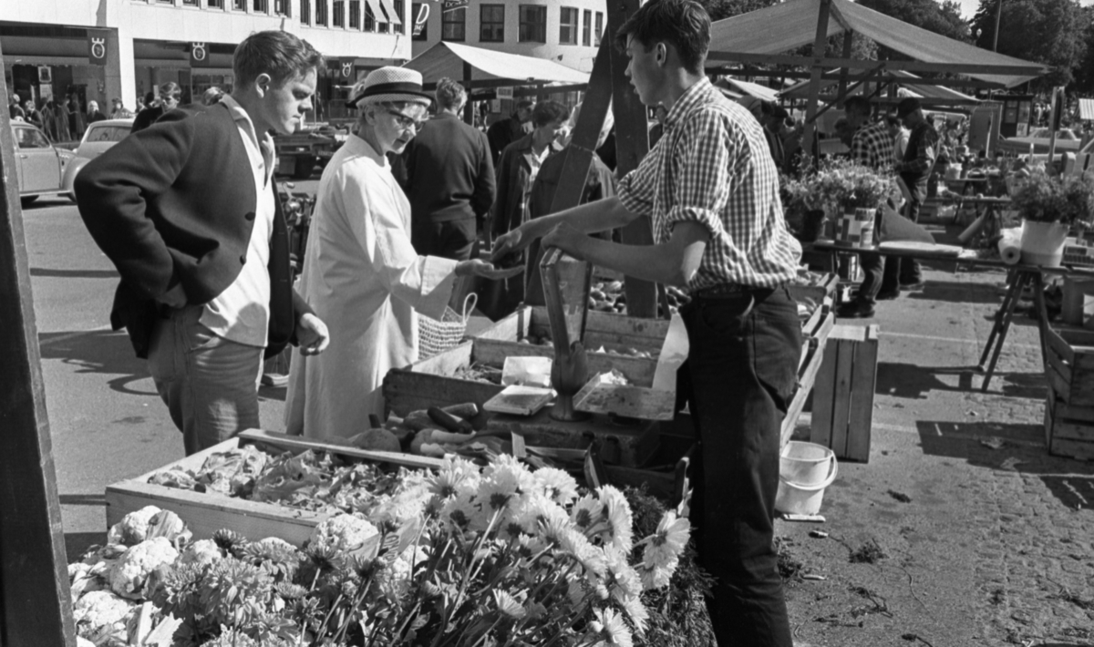 Torgreportage, 2 september 1965.
Information från Trädgårdsmästare Börje Eriksson: det är Börje som 17-åring som står i sin fars stånd och säljer bland annat krysantemum, blomkål och sallad.