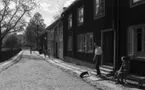 Wadköping, 28 maj 1966

Vy över Wadköping. En man med en tax kommer ut ur ett hus. En äldre kvinna sitter på en bänk invid huset. Enliten pojke kommer cyklande på gatan. Fler personer syns i bakgrunden av bilden.