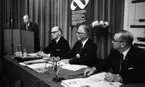 Orubricerad, Oscarianskt, Bara skämt, KF distrikt årsmöte 17 maj 1967

Fyra herrar i svarta kostymer, vita skjortor och mörka slipsar befinner sig i en lokal. En av dem står upp i en talarstol och tre sitter vid ett bord. De har liksom herrn vid talarstolen en mikroifon var framför sig. I bakgrunden finns en stor skylt med ett stort Konsummärke på och inunder står texten: 