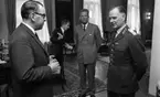 Kurator, Nye generalen 18 maj 1967

En ny general klädd i militäruniform står i en stor sal. Runtomkring honom befinner sig tre kostymklädda herrar.  Stolar och bord syns i bakgrunden. Mattor ligger på golvet. En stor spegel hänger på väggen i närheten av stora fönster.