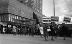 Första maj demonstration 2 maj 1967

Tre kvinnor går i förgrunden i ett första-majtåg utanför varuhuset Krämaren i Örebro. De är klädda i kappor och skor. Två av dem har hattar på huvudena. De bär skyltar med texten: 