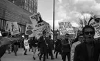 Första maj demonstration 2 maj 1967

Ett första-majtåg går genom centrala Örebro. Det passerar förbi varuhuset Krämaren. Många av personerna i tåget bär på demonstrationsskyltar med text. Många kvinnor är klädda i kappor och många män är klädda i rockar.