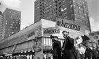 Första maj demonstration 2 maj 1967

Ett första-majtåg går genom centrala Örebro vid varuhuset Krämaren. I förgrunden syns tre män klädda i rockar och som bär på varsin demonstrationsskylt med texten: 